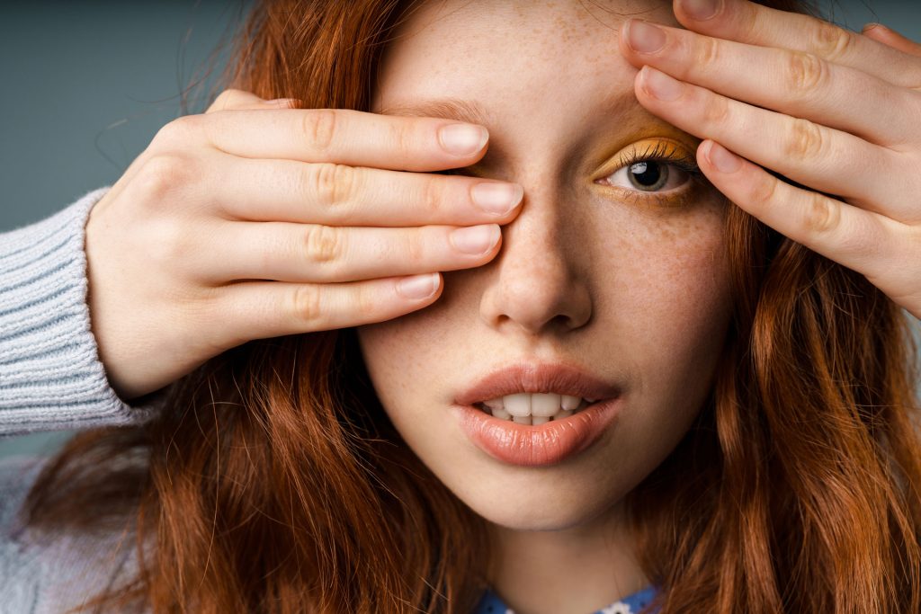 Young girl with red hair covering one of her eyes.