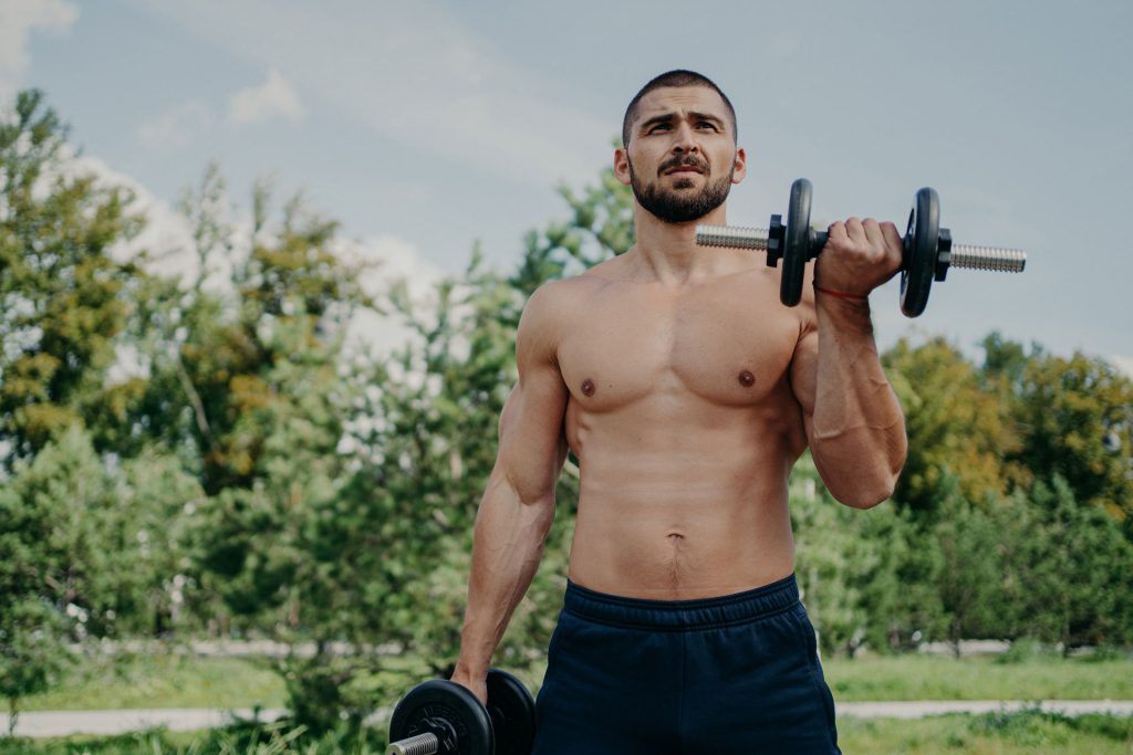 Muscular man outdoors doing bicep curls.
