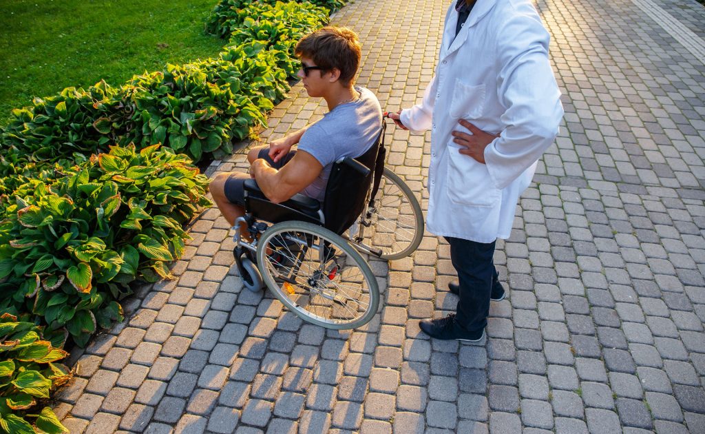 Young man in a wheelchair with his neuromuscular specialist doctor outdoor.