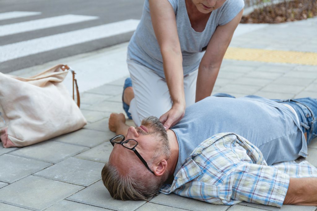 Helpful passerby checks the vital functions of a man lying in the ground.