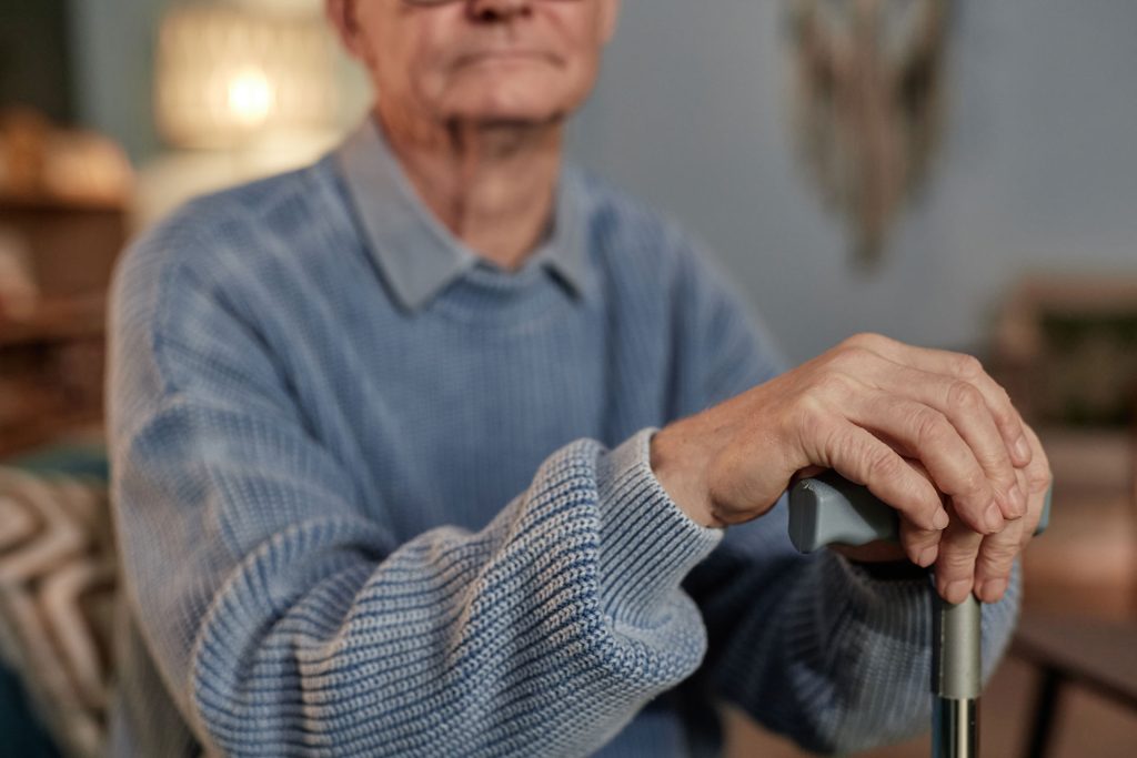 Elderly man sitting and holding a cane.