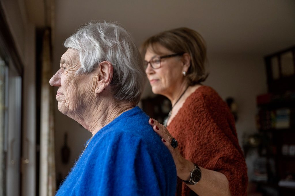 Two elderly friends standing looking outside.